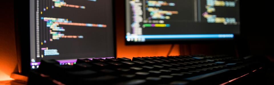 A keyboard and computer screens displaying code for software.