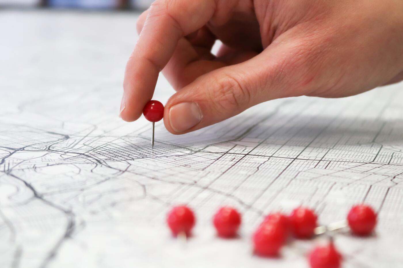 A hand placing a pin on a map.
