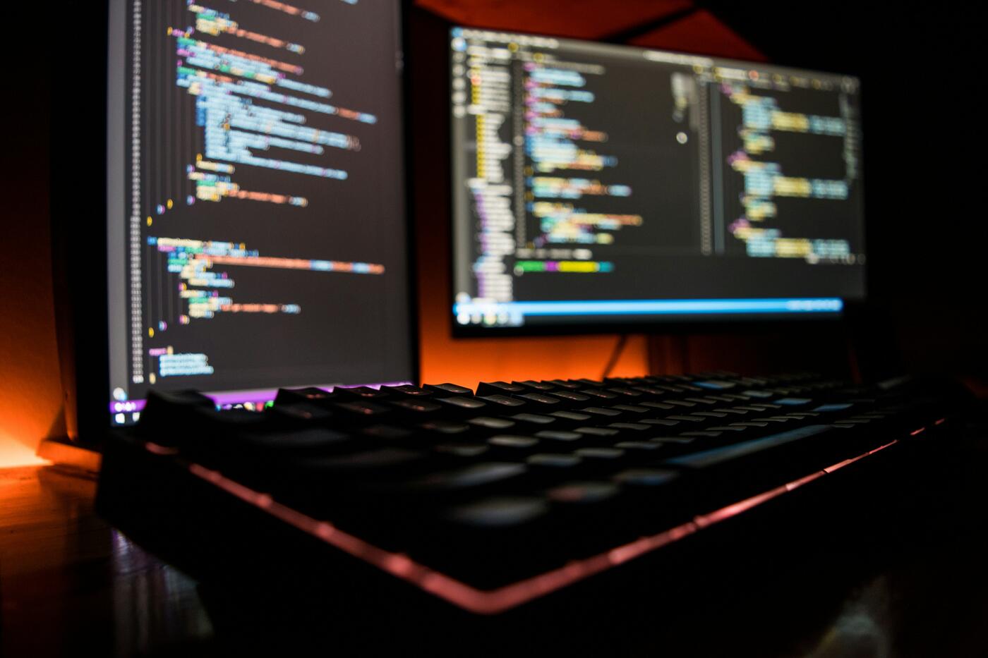 A keyboard and computer screens displaying code for software.