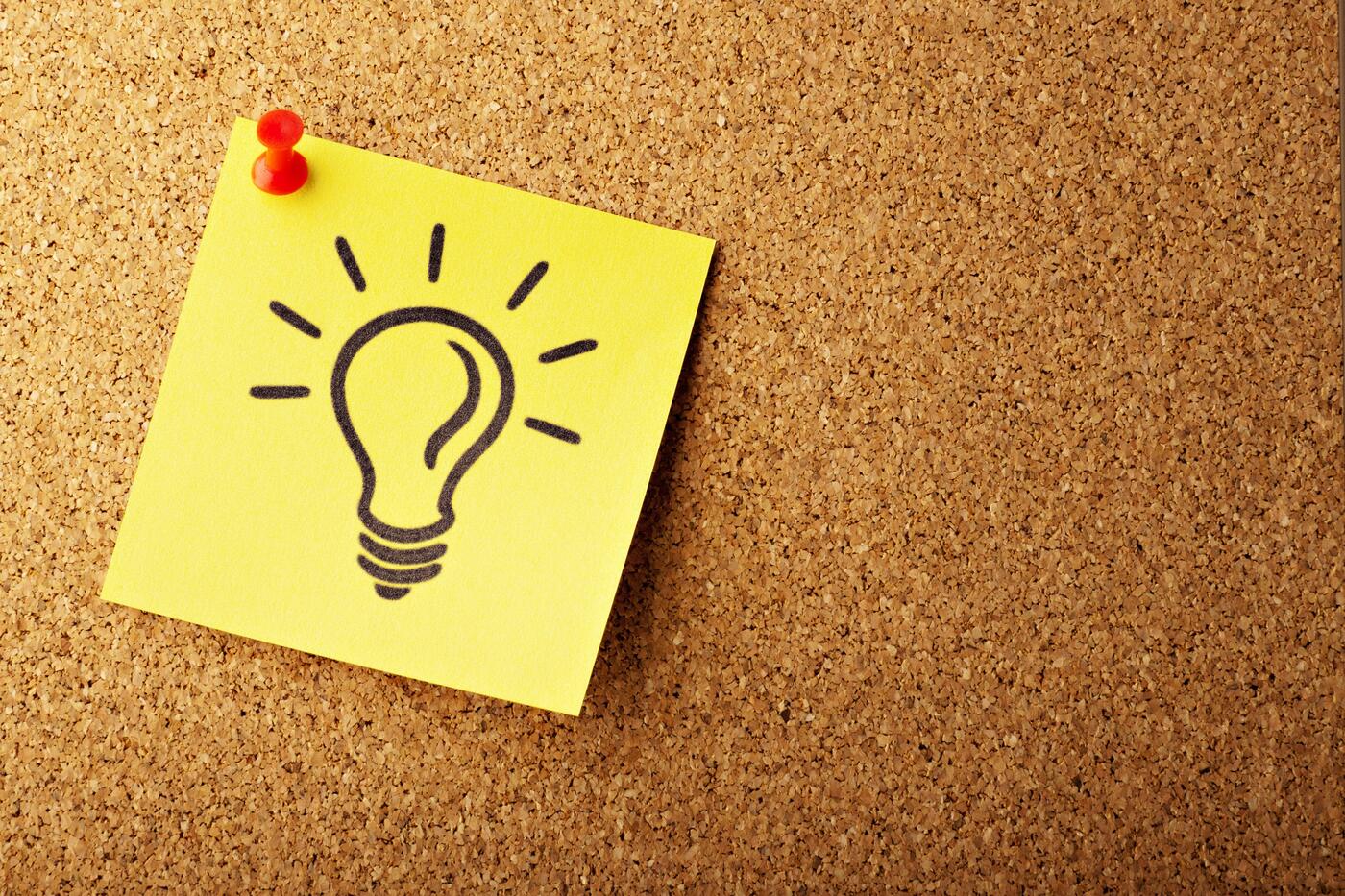 A lightbulb drawn on a sticky note. The sticky note is pinned to a corkboard.